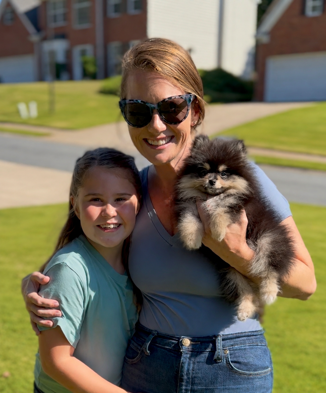 Mom and daughter smiling outdoors with their new black and tan Pomeranian puppy from Cream-Puffs