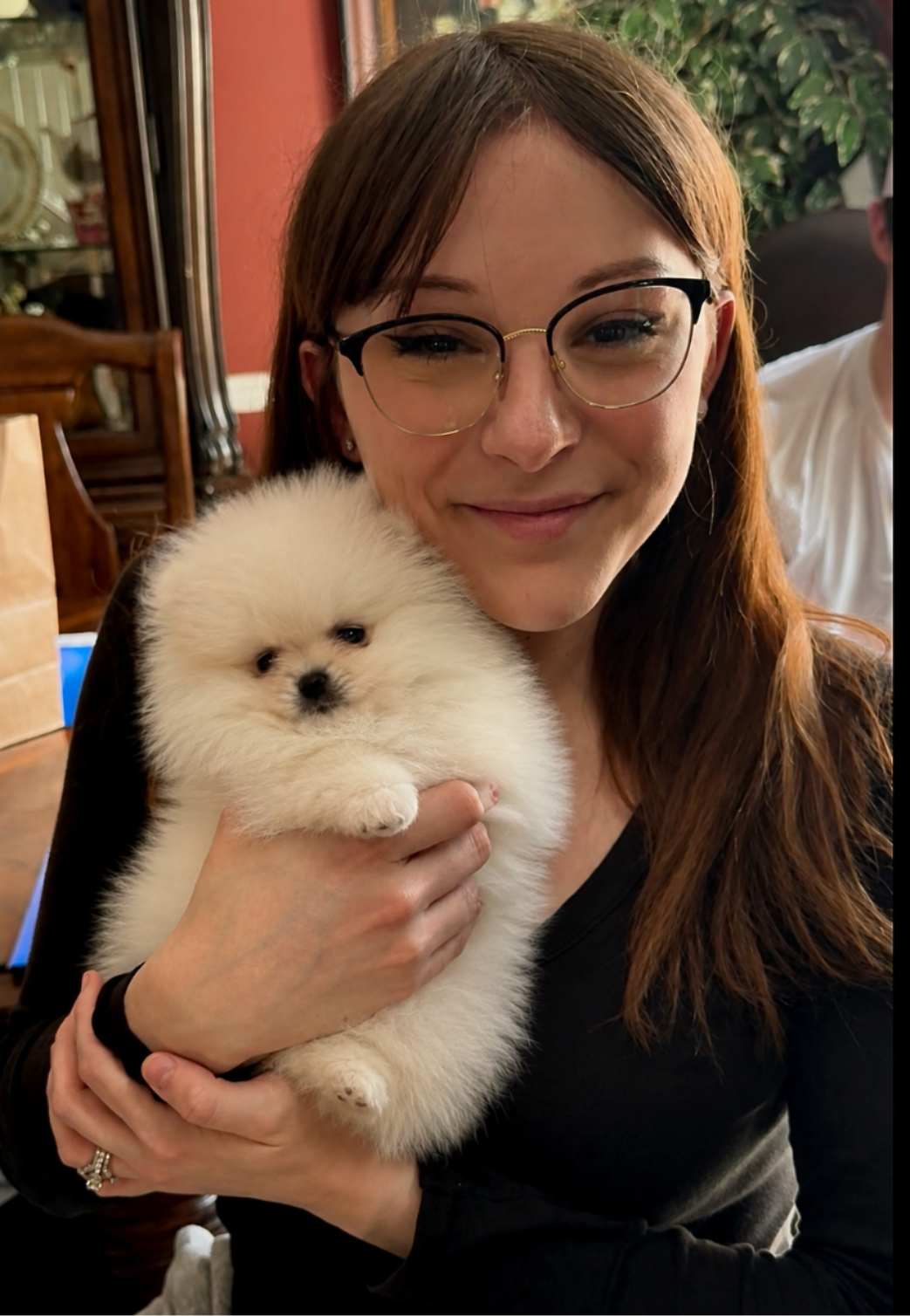 Young woman with glasses smiling while holding her fluffy white Pomeranian puppy from Cream-Puffs