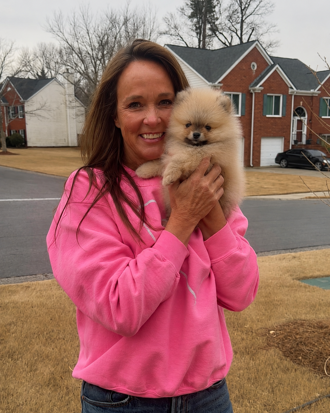Woman in pink sweatshirt holding her new cream Pomeranian puppy outside from Cream-Puffs