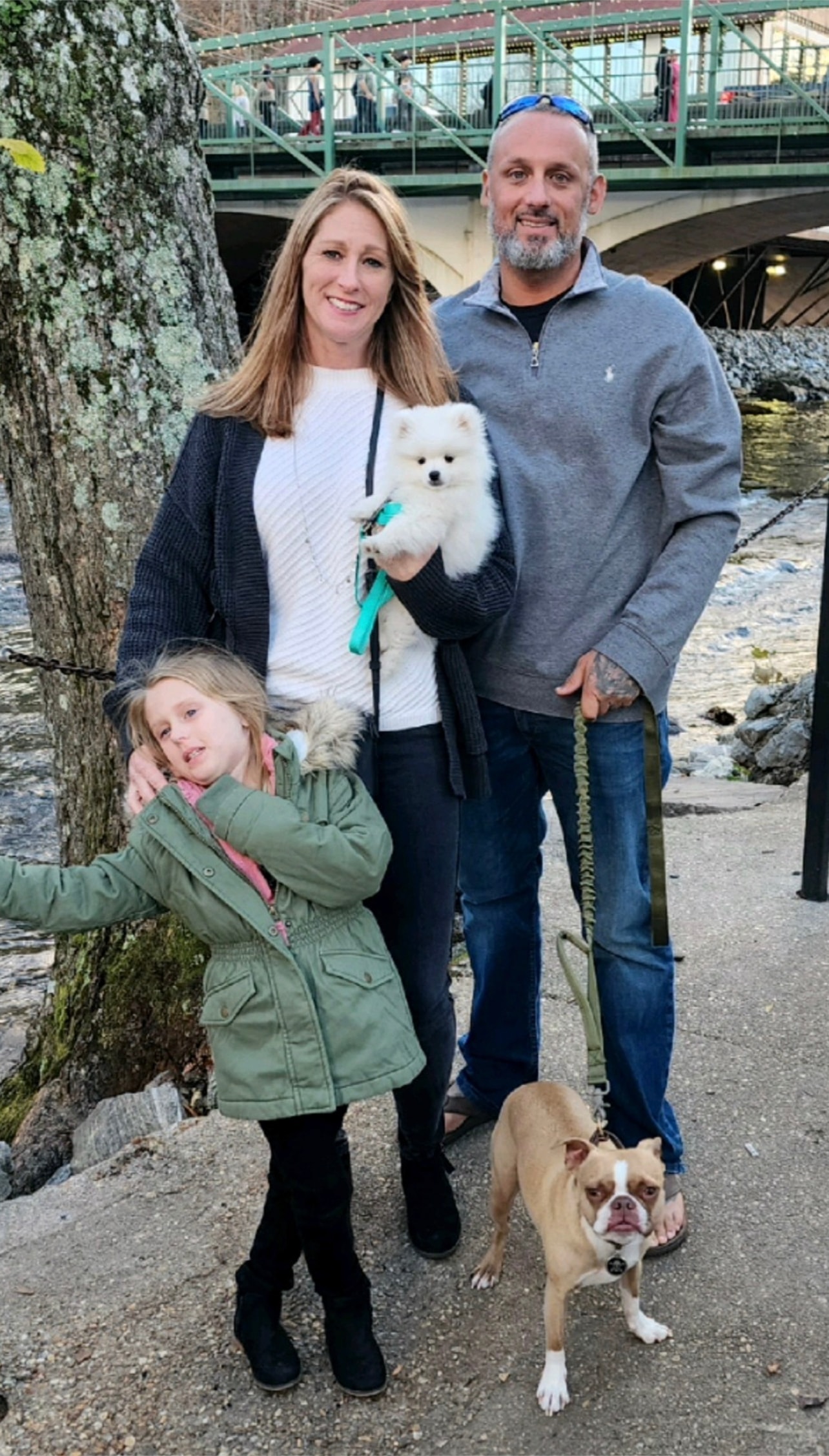 Family with mom holding white Pomeranian puppy and their dog by a bridge from Cream-Puffs