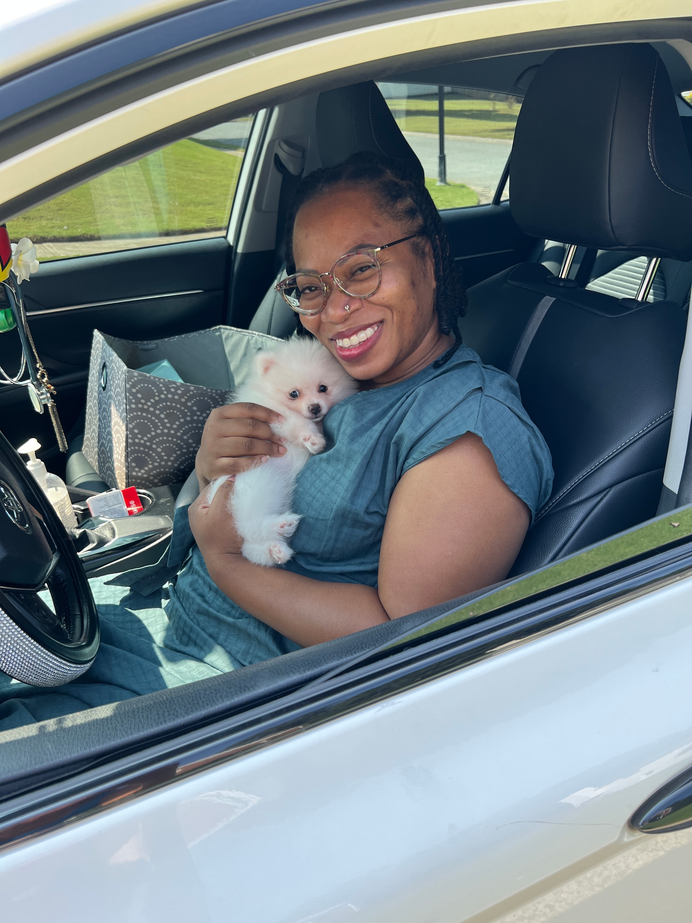 Woman with glasses smiling in her car holding her new white Pomeranian puppy from Cream-Puffs